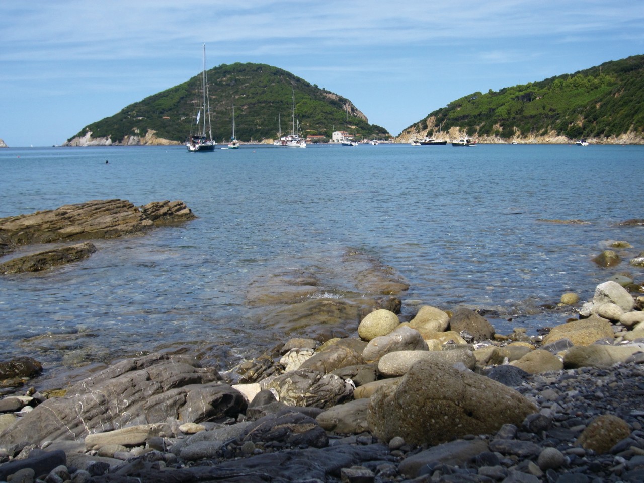 Plage de galets lisses et de rochers, baignée d'une eau cristalline, à Enfola.